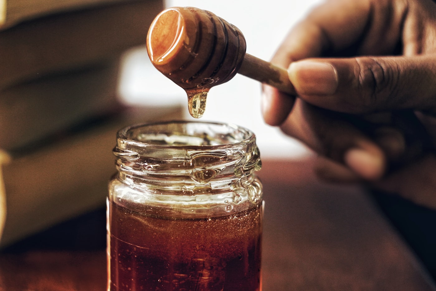 Pure honey dripping from a wooden dipper into a jar